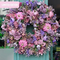 A large autumn-themed floral wreath in shades of pink, lilac, and gold, decorated with faux pumpkins and dense flowers, hanging on a teal door.