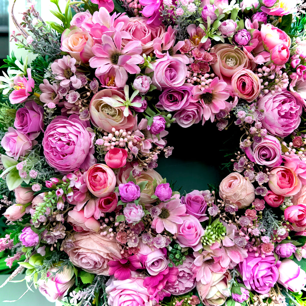close up of a pink artificial floral wreath full of various flowers including roses, ranunculus and daisies