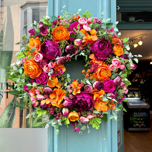 full front view of our cranorange artificial wreath, with vibrant orange ranunculus and deep cranberry peonies by jamesia blooms