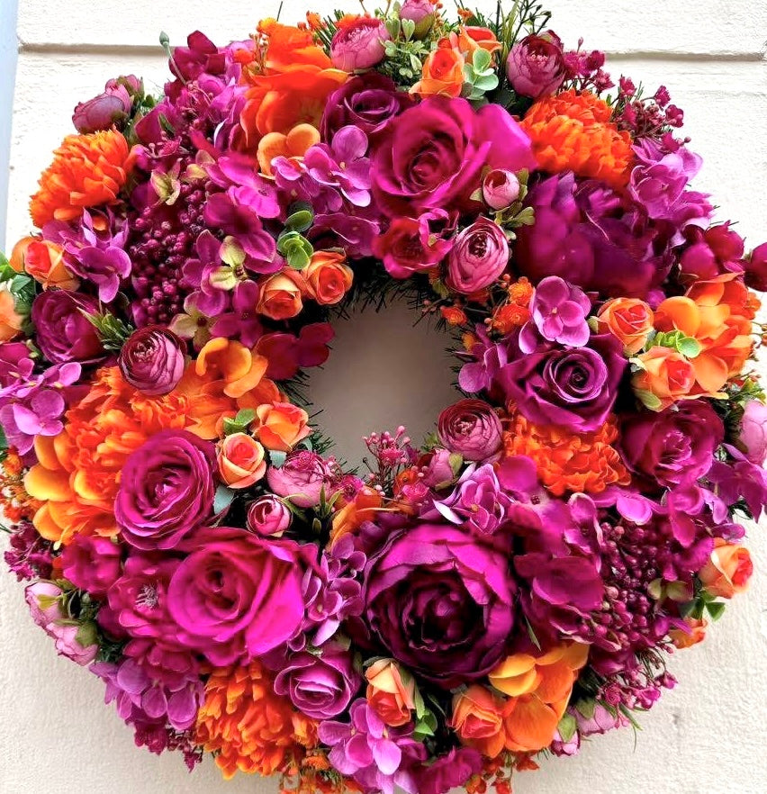Colorful artificial flower wreath with pink, orange, and purple flowers on a white background, jamesia blooms favorite summer seller