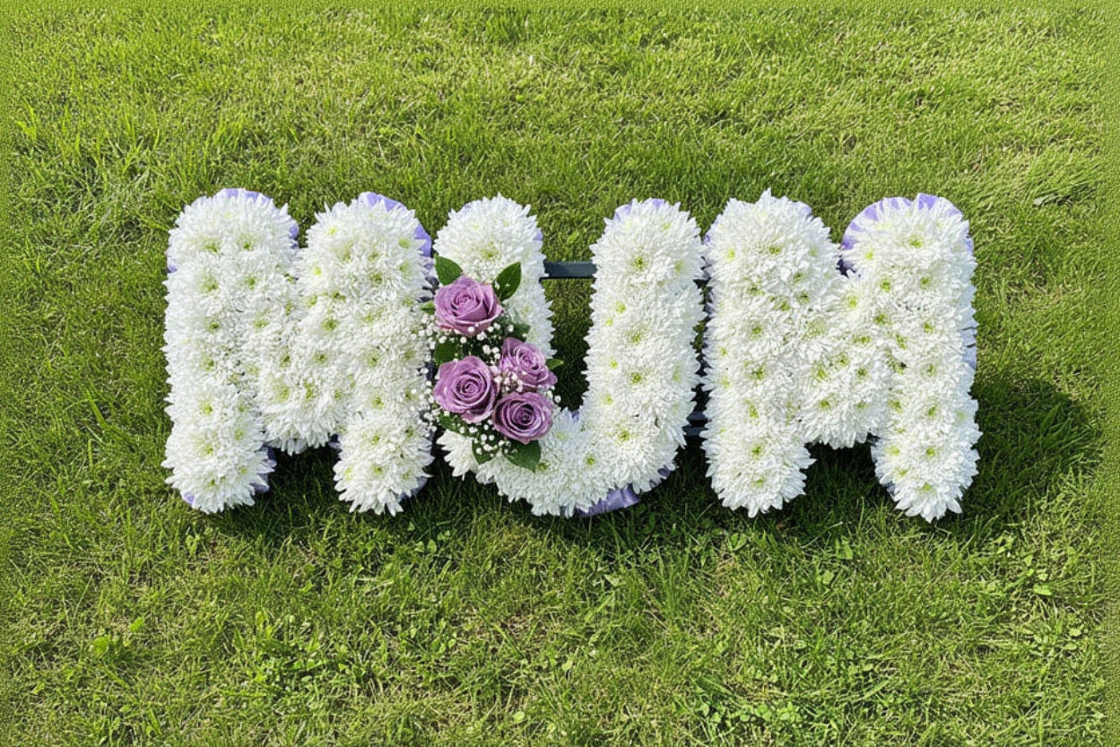 White Fresh flower funeral tribute, spelling out 'MUM'  with a spray of lilac roses on a grassy background