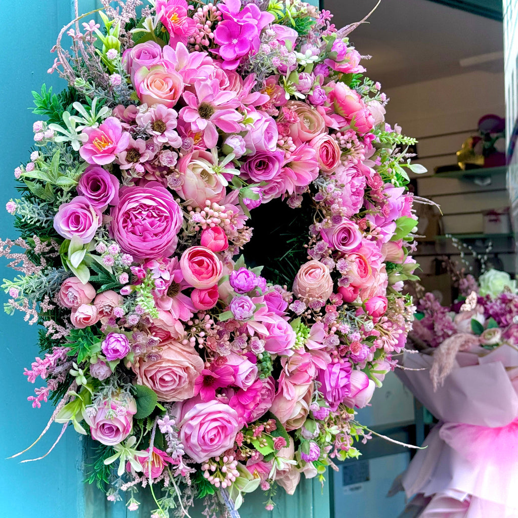 The Pink One by jamesia blooms, a side view of a full pink artificial wreath hanging on a store front 