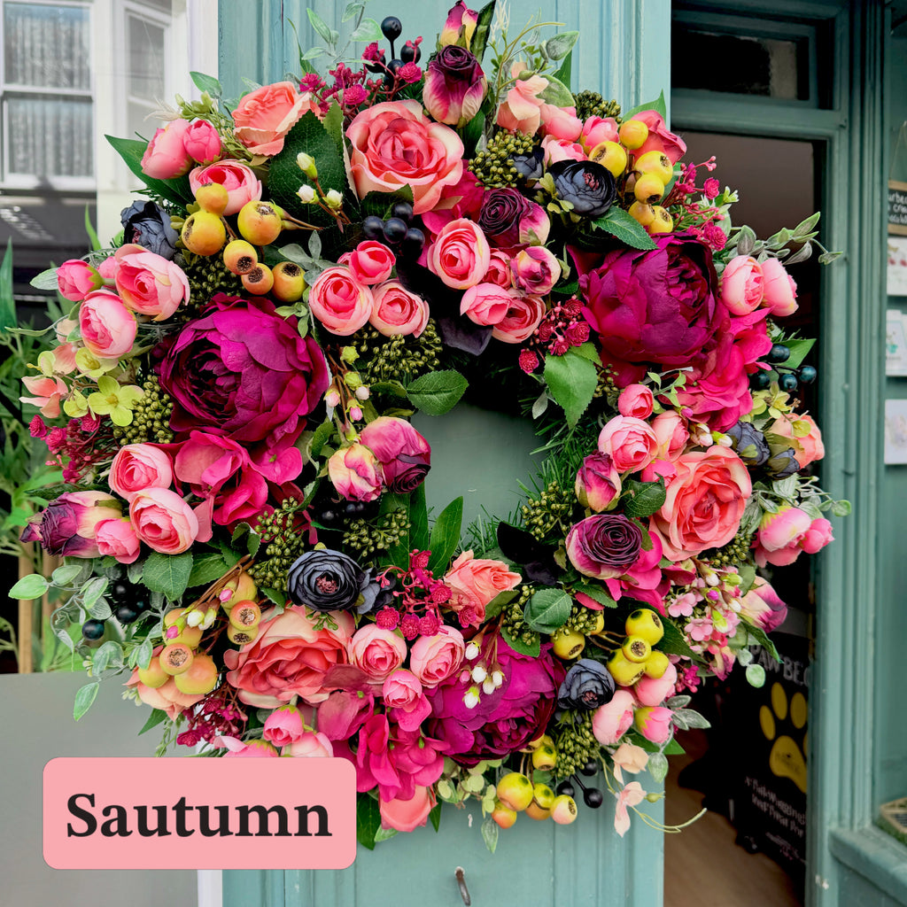Artificial floral wreath hanging on a shop front. Pink, coral, magenta And black flowers with green berries on a spruce base.