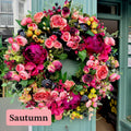 Artificial floral wreath hanging on a shop front. Pink, coral, magenta And black flowers with green berries on a spruce base.