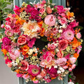 Colorful floral wreath, fruit salad inspired with white, lemon, orange, pink and green faux flowers and berries, hanging on a shop front