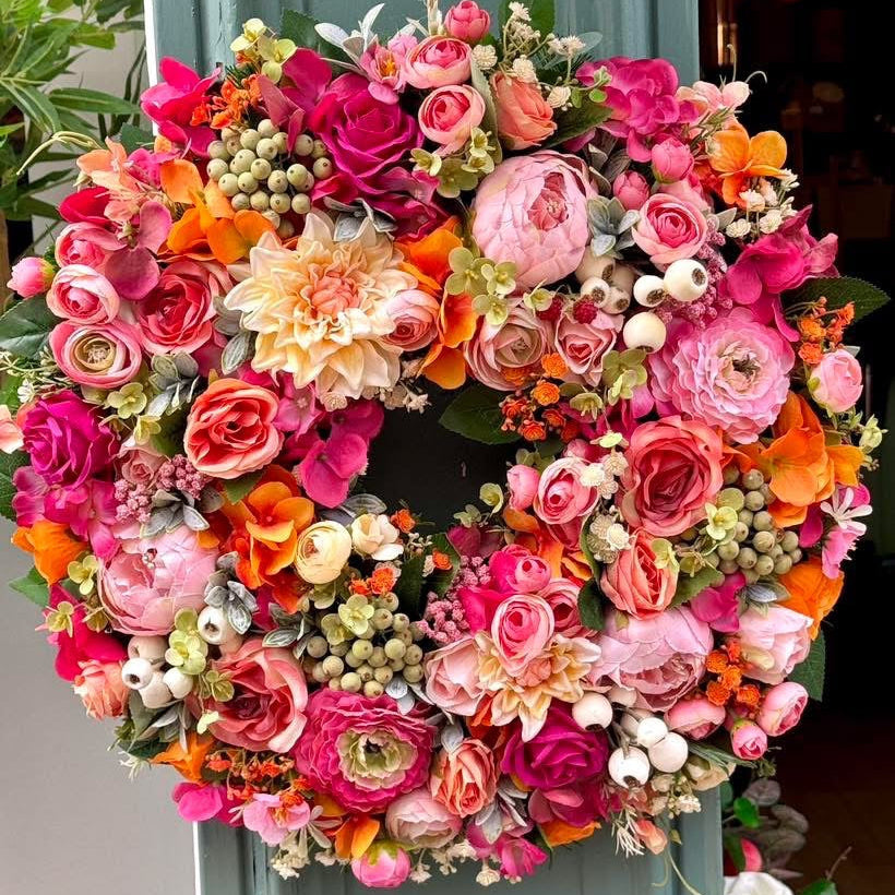 Colorful floral wreath, fruit salad inspired with white, lemon, orange, pink and green faux flowers and berries, hanging on a shop front