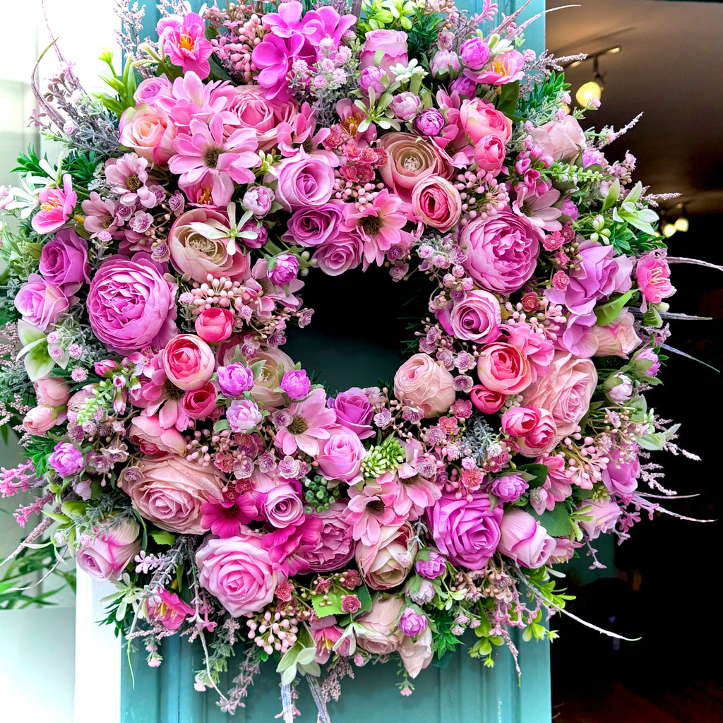 artificial all year round wreath full of various toned pink flowers including roses ranunculus and daisies