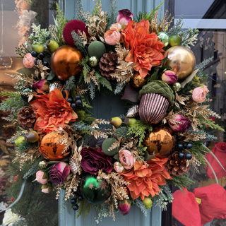 christmas woodland themed wreath, with orange dahlias, orange, brown, green and gold baubles with an acorn bauble and burgundy flowers
